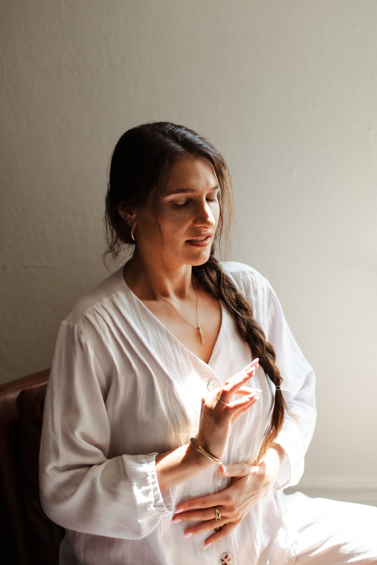 Amira sitting with one hand on her heart and one on her belly, eyes lowered